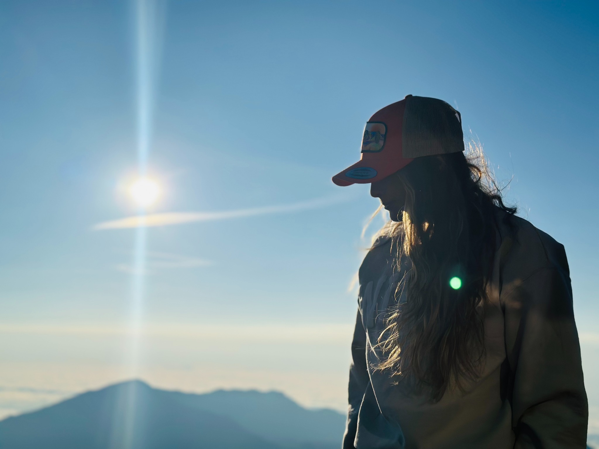 Jess standing in silhouette against a bright mountain sky