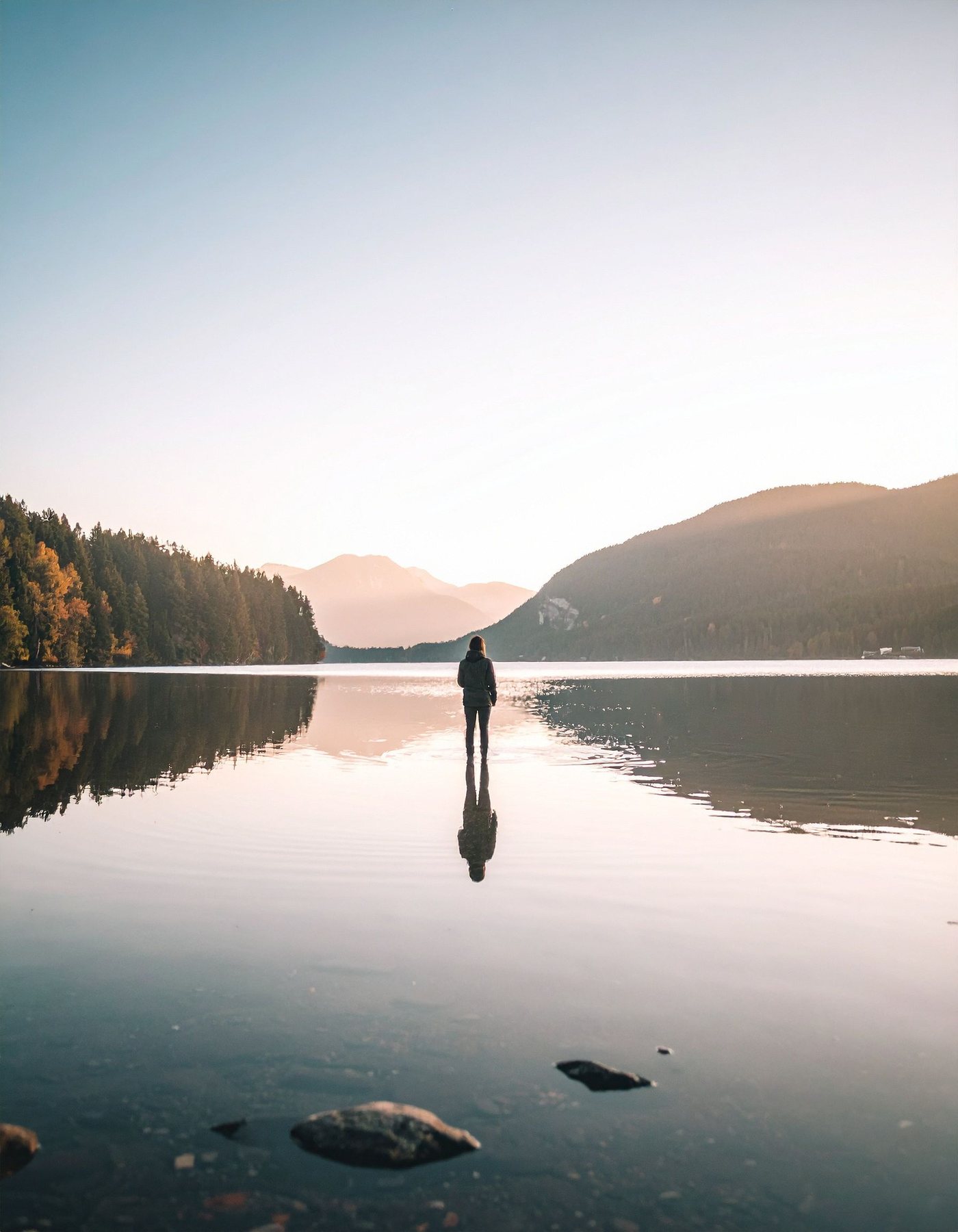 A person standing quietly in the still water of a mountain lake